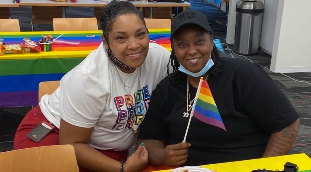 Two smiling african american women at an LGBTQ+ event. One is holding a rainbow flag