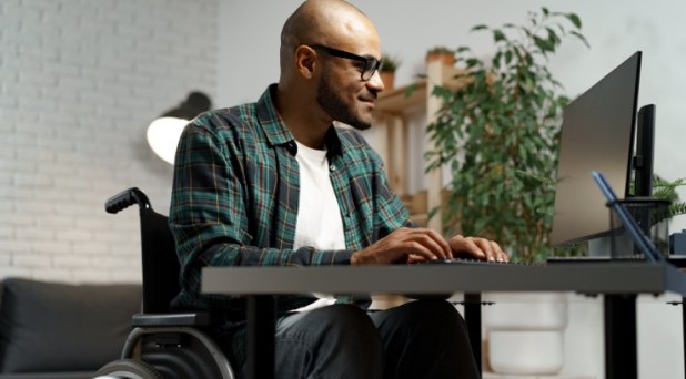 Disabled young african american man in wheelchair using computer while sitting at his working table